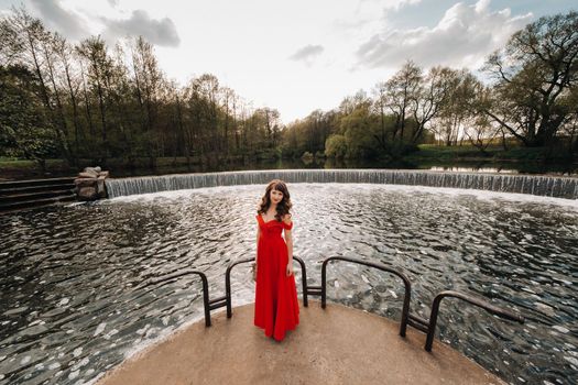 girl in a long red dress near the lake in the Park at sunset