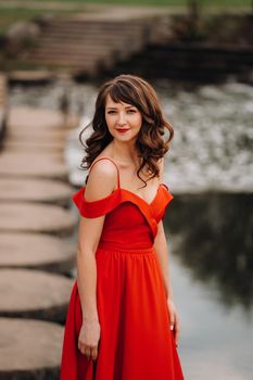 girl in a long red dress near the lake in the Park at sunset