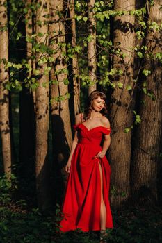 Spring Portrait of a laughing girl in a long red dress with long hair walking in the Park in the woods