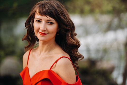 portrait of a young beautiful girl with long brown hair, in a long red dress in nature.