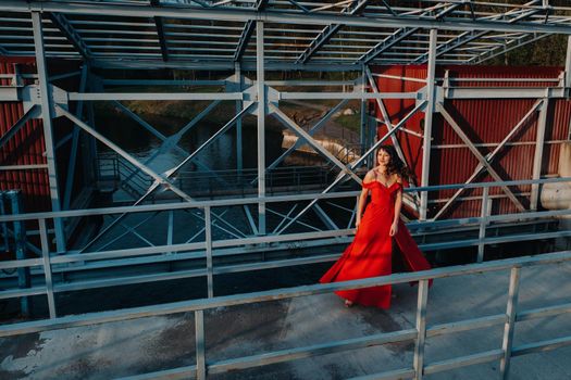 A girl in a red dress on a dam near a river at sunset.