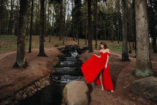 Spring Portrait of a laughing girl in a long red dress with long hair walking in the Park in the woods