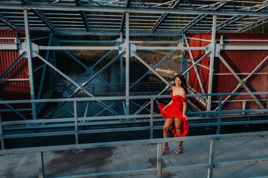 A girl in a red dress on a dam near a river at sunset.