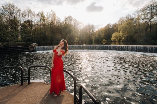 girl in a long red dress near the lake in the Park at sunset