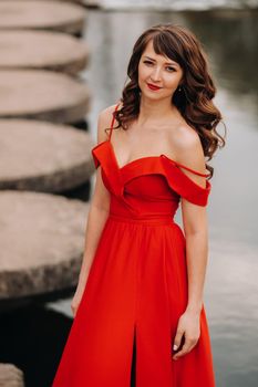 girl in a long red dress near the lake in the Park at sunset