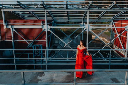 A girl in a red dress on a dam near a river at sunset.