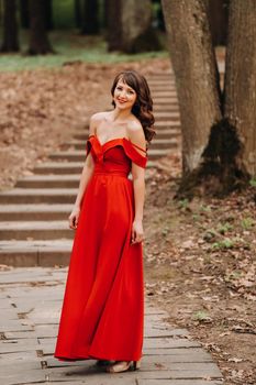 Spring Portrait of a laughing girl in a long red dress with long hair walking in the Park in the woods