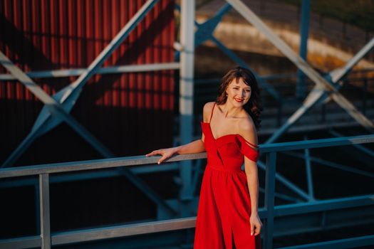 A girl in a red dress on a dam near a river at sunset.