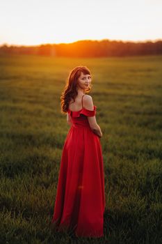 a beautiful girl in spring in a red dress is walking in a field at sunset. Taken from the air by a quadrocopter.