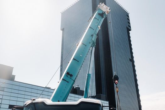 blue crane lifting mechanism with hooks near the glass modern building, crane and hydraulic high lift up to 120 meters.