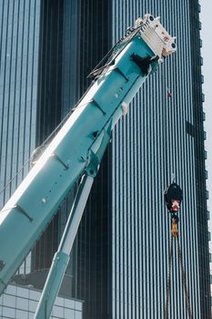 blue crane lifting mechanism with hooks near the glass modern building, crane and hydraulic high lift up to 120 meters.