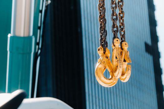 The hooks of the mobile crane near the glass of high buildings.Lots of hooks hanging from chains suspended from a crane.