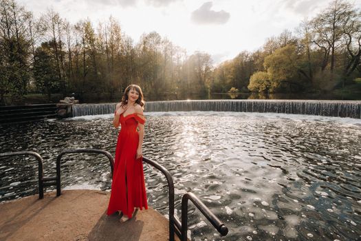 girl in a long red dress near the lake in the Park at sunset