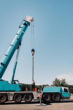 the counterweight is installed by an unrecognizable worker on a large blue car crane and is prepared to work on a site next to a large modern building. The largest truck crane for solving complex tasks.