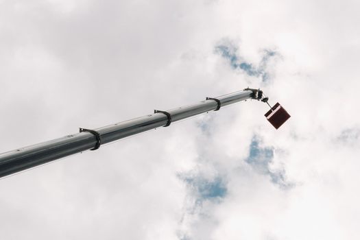 Raised high in the sky cradle of a car crane. The tallest truck crane with a yellow cradle for solving complex tasks.