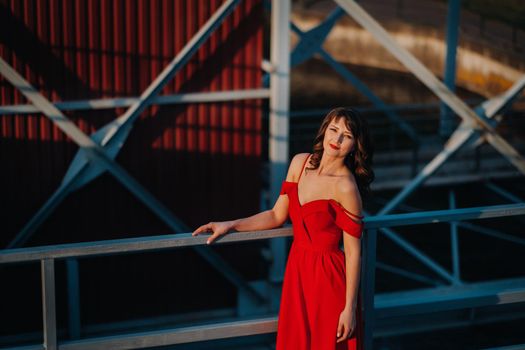 A girl in a red dress on a dam near a river at sunset.