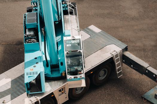 a cab with the operator of a Large blue car crane that stands ready to operate on hydraulic supports on a platform next to a large modern building. The largest truck crane for solving complex tasks