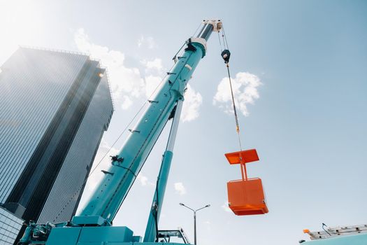 A large blue truck crane stands ready for operation on a site near a large modern building. The largest truck crane with a yellow cradle for solving complex tasks.