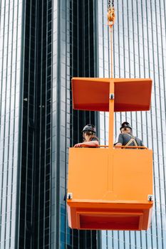 Workers in a construction cradle climb on a crane to a large glass building.The crane lifts the workers in the car seat.Construction.