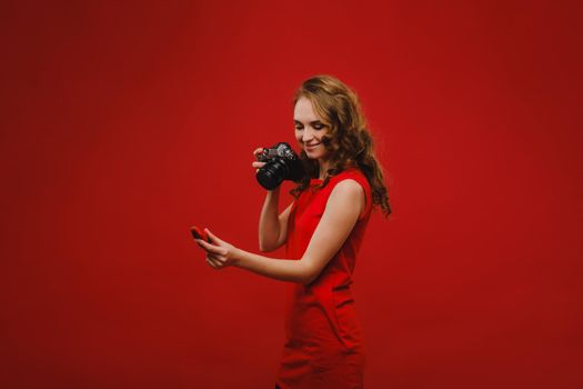 a smiling young woman with wavy hair holds a strawberry and photographs it, holding a delicious fresh strawberry on a bright red background.