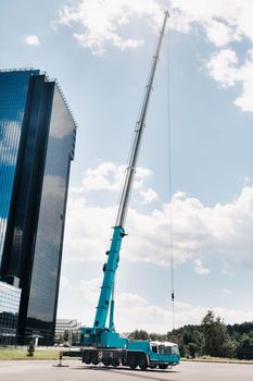 the tallest and largest blue car crane is laid out on a platform next to a large modern building. The largest truck crane for complex tasks.