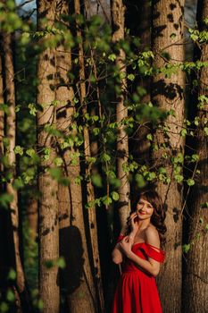 Spring Portrait of a laughing girl in a long red dress with long hair walking in the Park in the woods