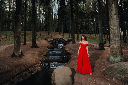 Spring Portrait of a laughing girl in a long red dress with long hair walking in the Park in the woods