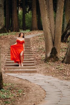 Spring Portrait of a laughing girl in a long red dress with long hair walking in the Park in the woods