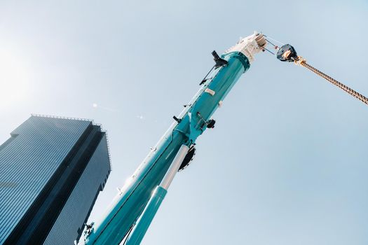 blue crane lifting mechanism with hooks near the glass modern building, crane and hydraulic high lift up to 120 meters.