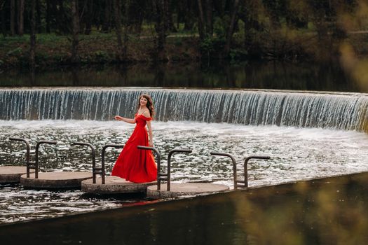 girl in a long red dress near the lake in the Park at sunset