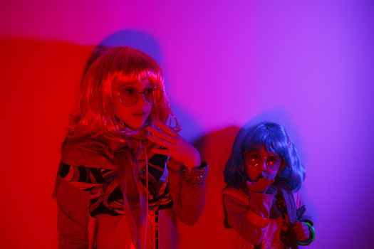 Two little girls wearing a colorful wig and heart-shaped sunglasses posed for a photo shooting on the disco light background