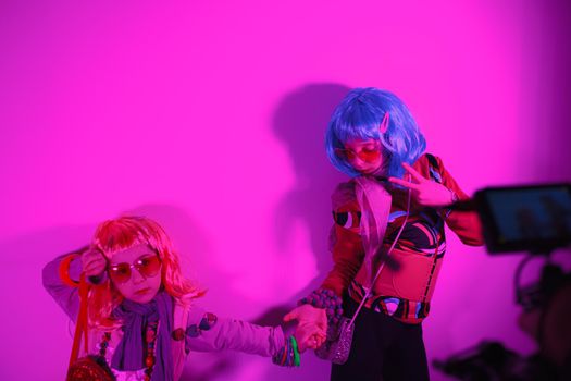 Little girls wearing a colorful wig and heart-shaped sunglasses posed for a photo shooting on the disco light background