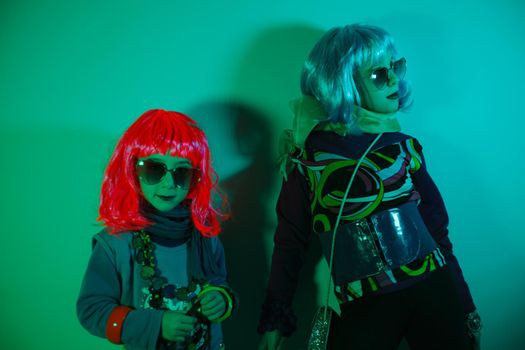 Portrait of a glamour little girls wearing colorful wig and heart shaped sunglasses on green background