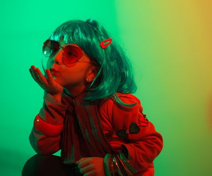 A glamour little girl posing for a photo portrait while wearing a colorful wig on green background