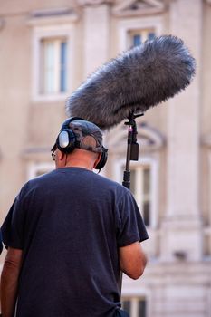 Behind the scene. Sound recorder with microphone, boom mic and headphones filming movie scene on outdoor location