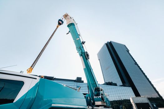 blue crane lifting mechanism with hooks near the glass modern building, crane and hydraulic high lift up to 120 meters.