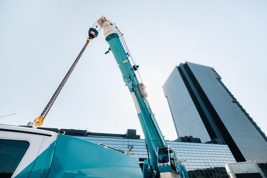 blue crane lifting mechanism with hooks near the glass modern building, crane and hydraulic high lift up to 120 meters.