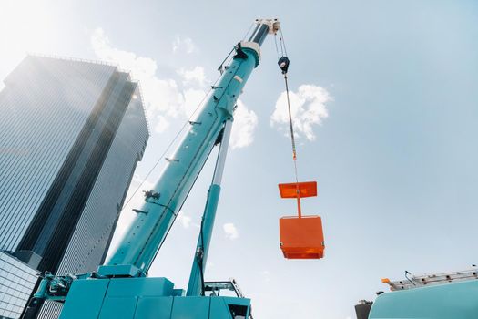 A large blue truck crane stands ready for operation on a site near a large modern building. The largest truck crane with a yellow cradle for solving complex tasks.