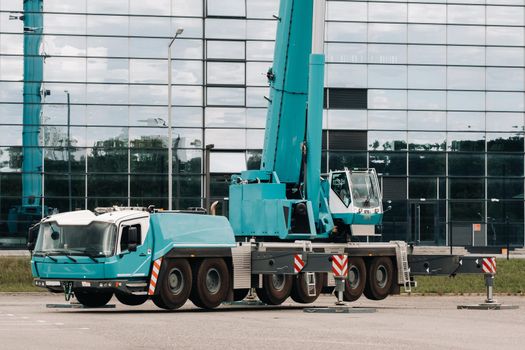 A large blue truck crane stands ready to operate on hydraulic supports on a platform next to a large modern building. The largest truck crane for solving complex tasks