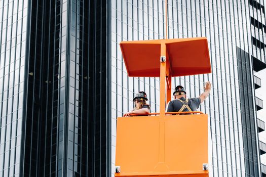 Workers in a construction cradle climb on a crane to a large glass building.The crane lifts the workers in the car seat.Construction.