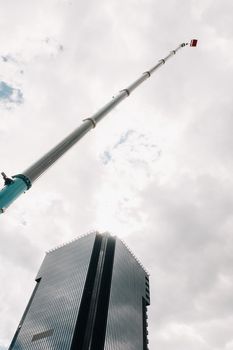 A large blue truck crane stands ready for operation on a site near a large modern building. The largest truck crane with a yellow cradle for solving complex tasks.