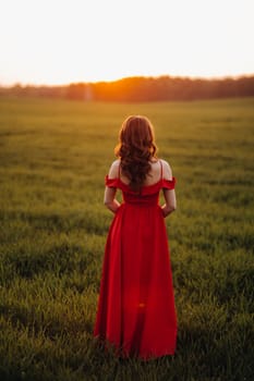 a beautiful girl in spring in a red dress is walking in a field at sunset. Taken from the air by a quadrocopter.