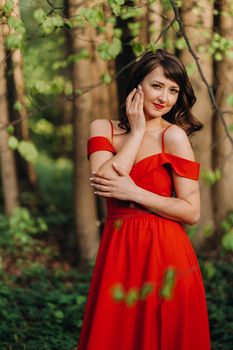 Spring Portrait of a laughing girl in a long red dress with long hair walking in the Park in the woods