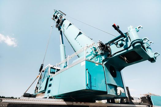 a cab with the operator of a Large blue car crane that stands ready to operate on hydraulic supports on a platform next to a large modern building. The largest truck crane for solving complex tasks