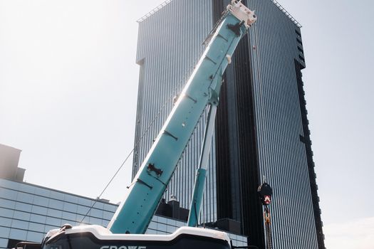 blue crane lifting mechanism with hooks near the glass modern building, crane and hydraulic high lift up to 120 meters.