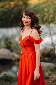 girl in a long red dress near the lake in the Park at sunset