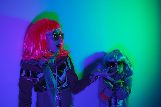 Two little girls wearing a colorful wig and heart-shaped sunglasses posed for a photo shooting on the disco light background