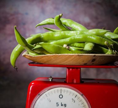 View of fresh broad beans on the weight scale in a wooden table