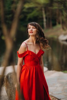 a young beautiful girl with long brown hair, in a long red dress with a ring around the lake.