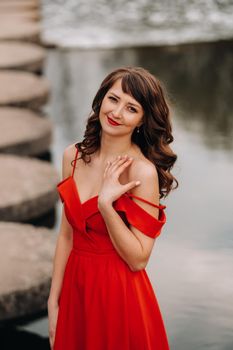 girl in a long red dress near the lake in the Park at sunset